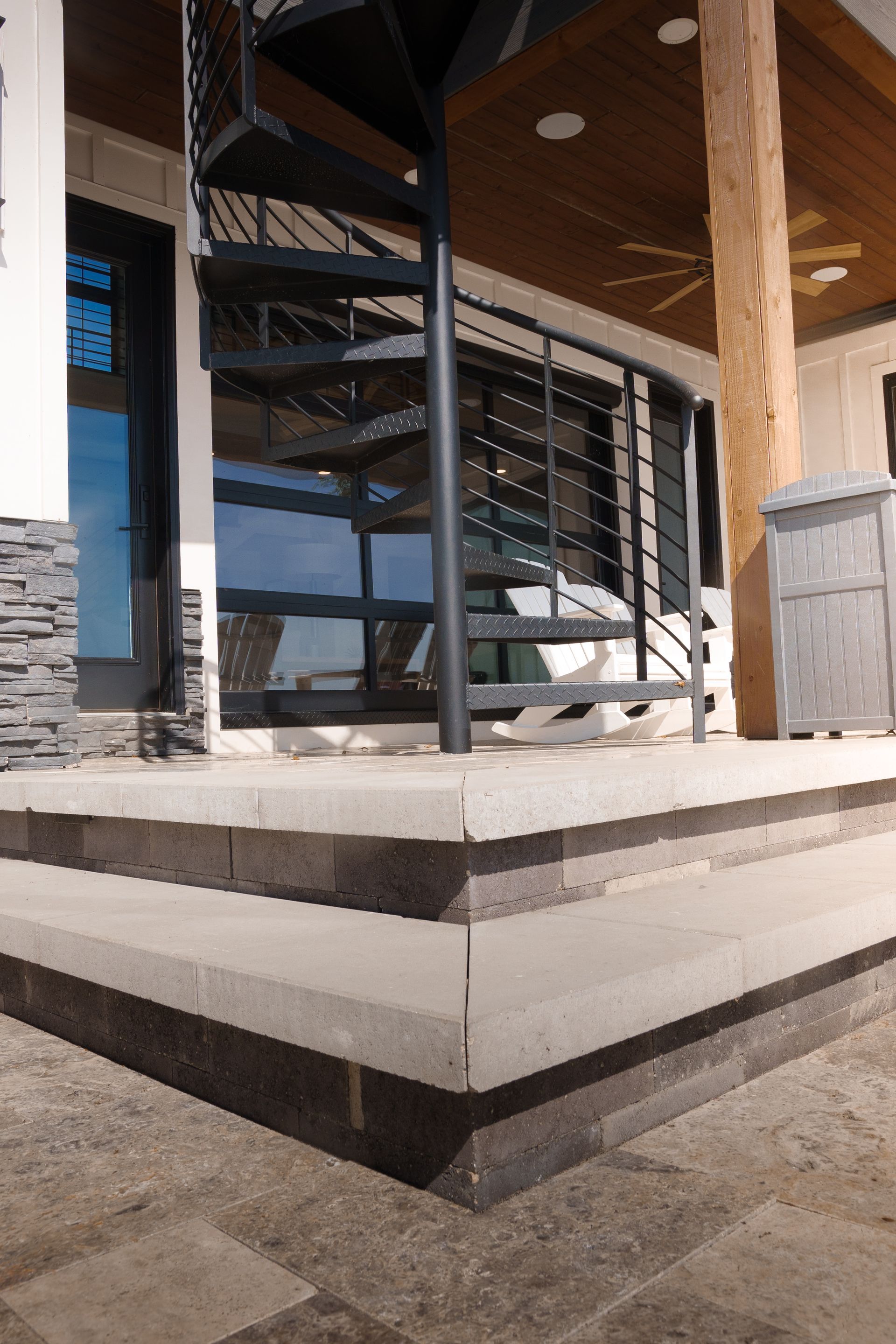 Exterior view of steps leading to a building with a spiral staircase. Gray concrete steps lead up to a glass and black metal structure.