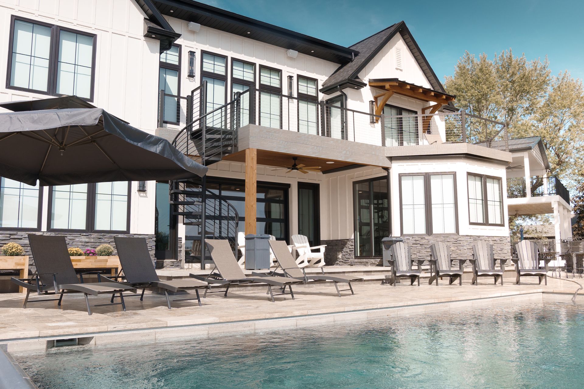 Modern two-story home with a pool. The house has white siding, black trim, and multiple balconies, with lounge chairs by the pool.