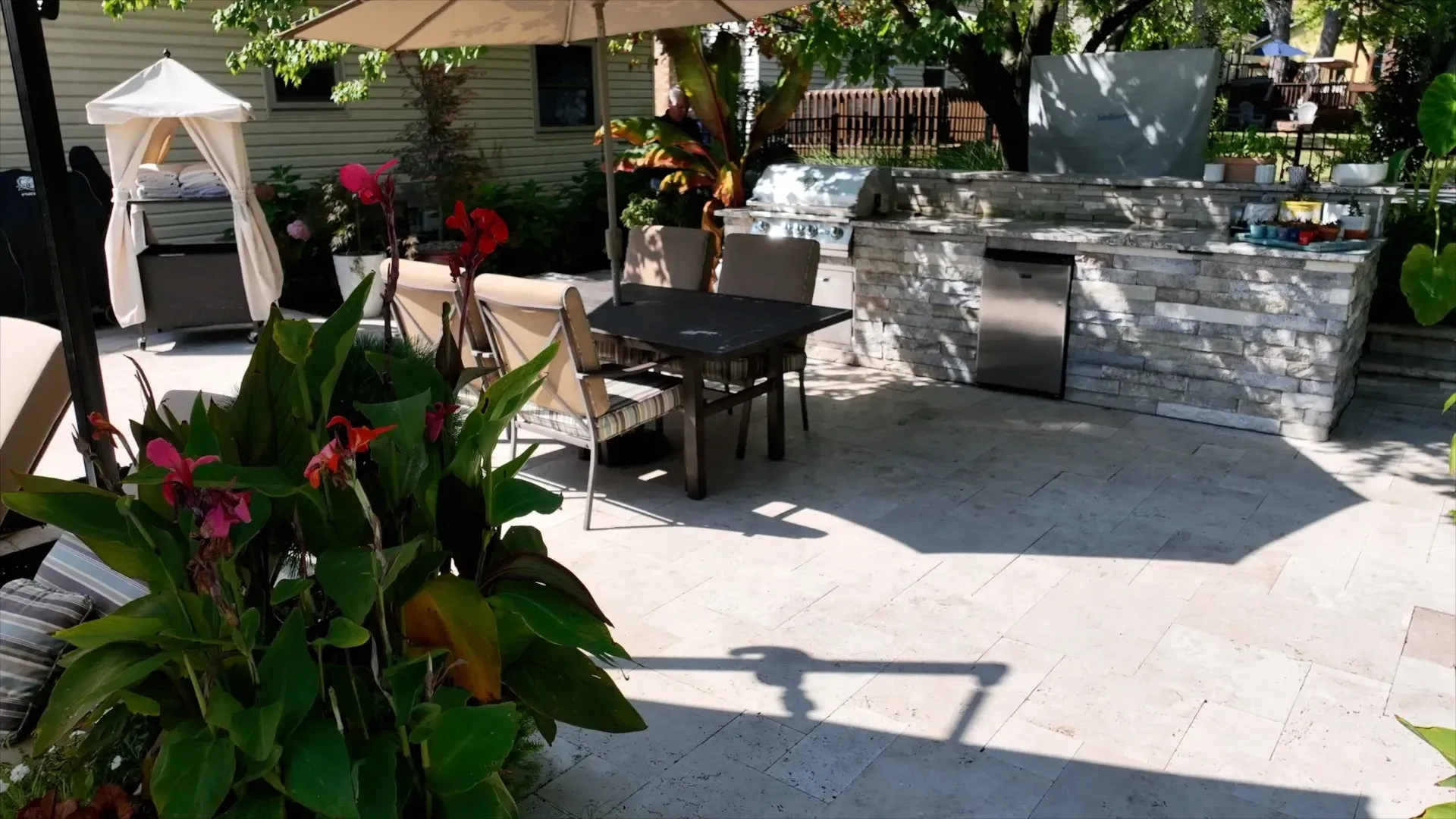 Outdoor kitchen and dining area with a stone countertop, table and chairs, and lush green plants.