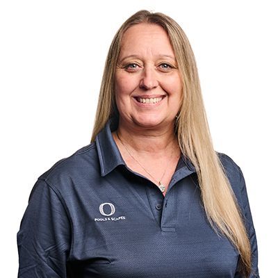 Woman with long blonde hair smiles, wearing a dark blue collared shirt with a logo on the left. White background.