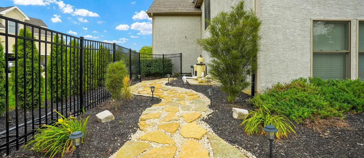 A stone pathway leading to a house surrounded by beautiful landscaping.