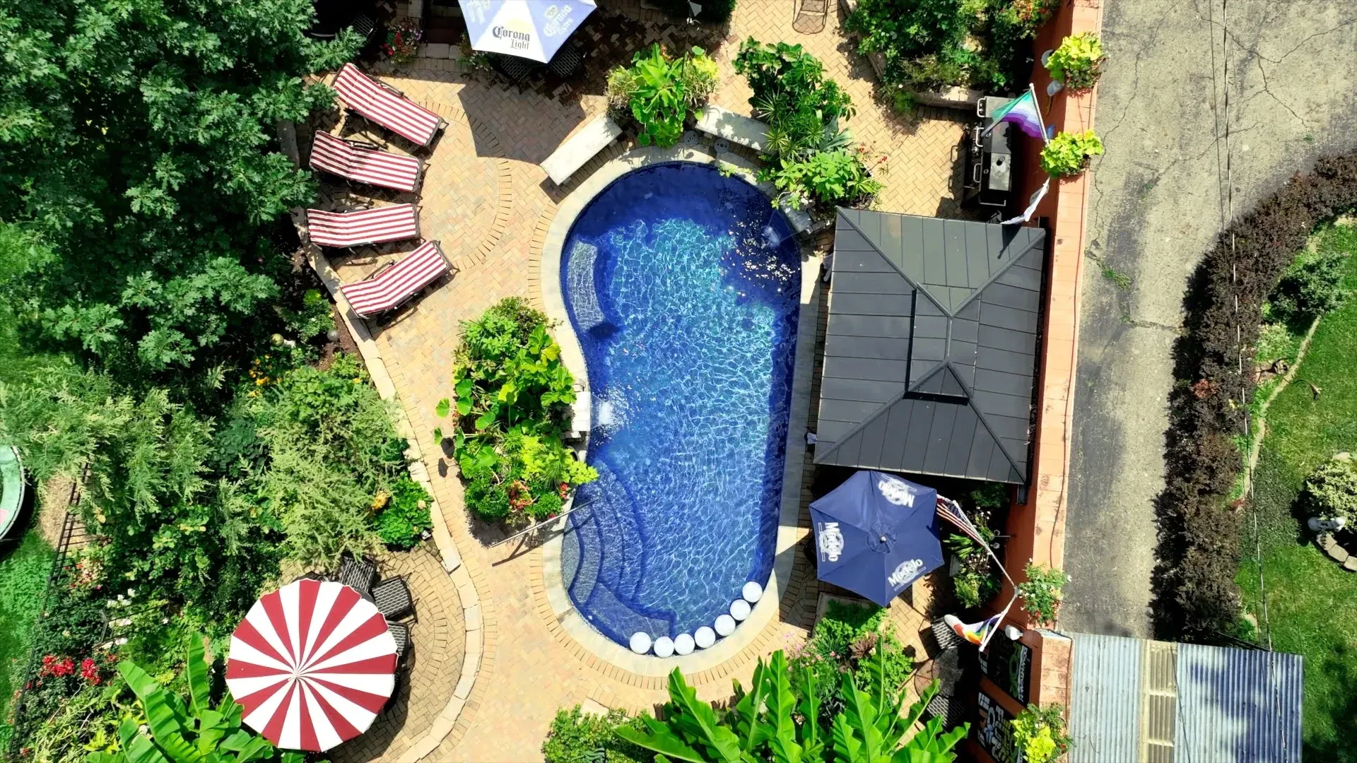 Overhead view of a resort pool shaped like a foot. Lounge chairs, a gazebo, and umbrellas surround the pool, set in a lush, green landscape.