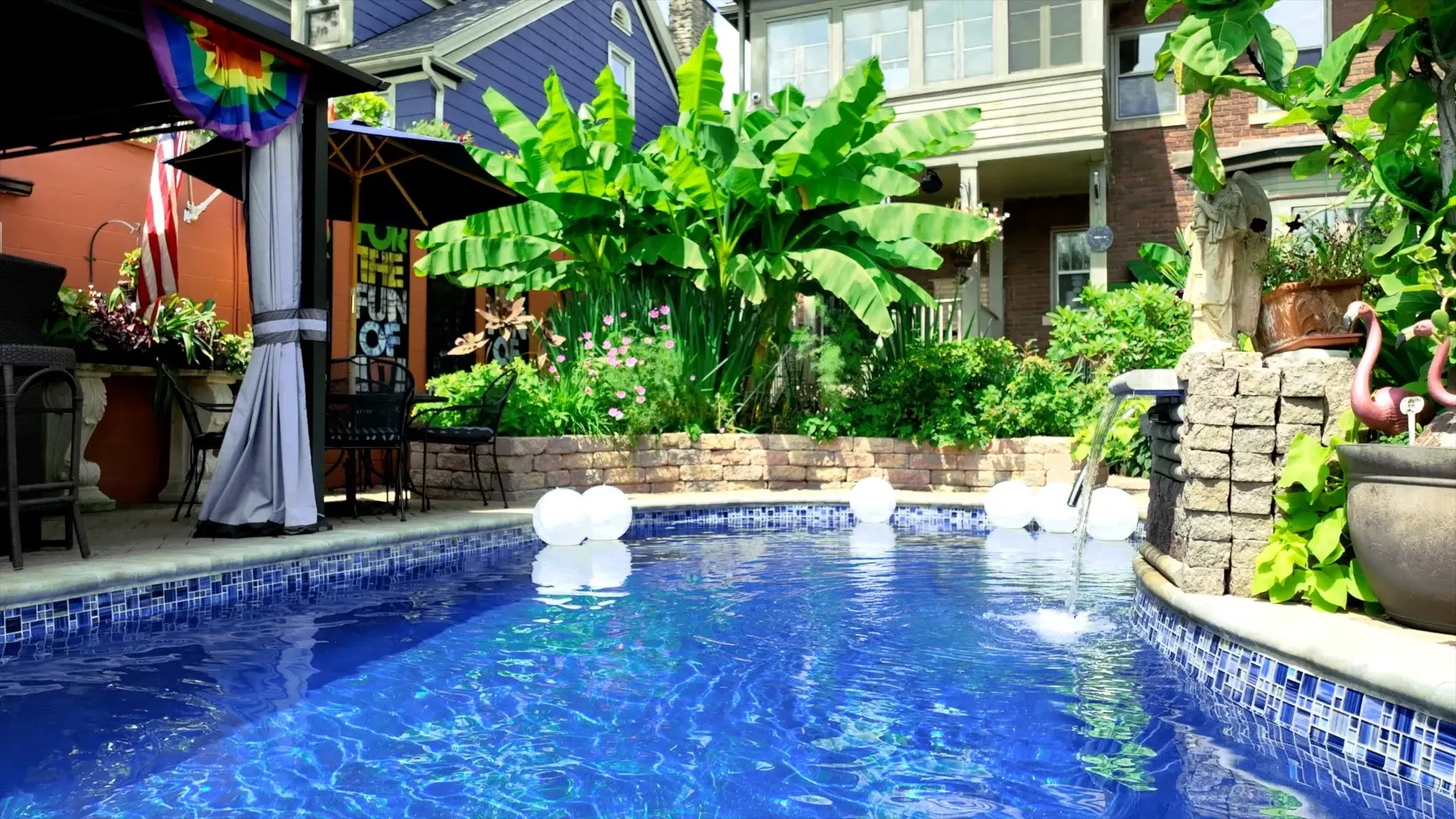 Swimming pool in a backyard oasis with lush greenery, a gazebo, and white orbs floating on the water.