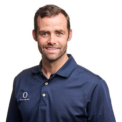 Man with short brown hair and a light beard wearing a navy blue polo shirt smiles at the camera.