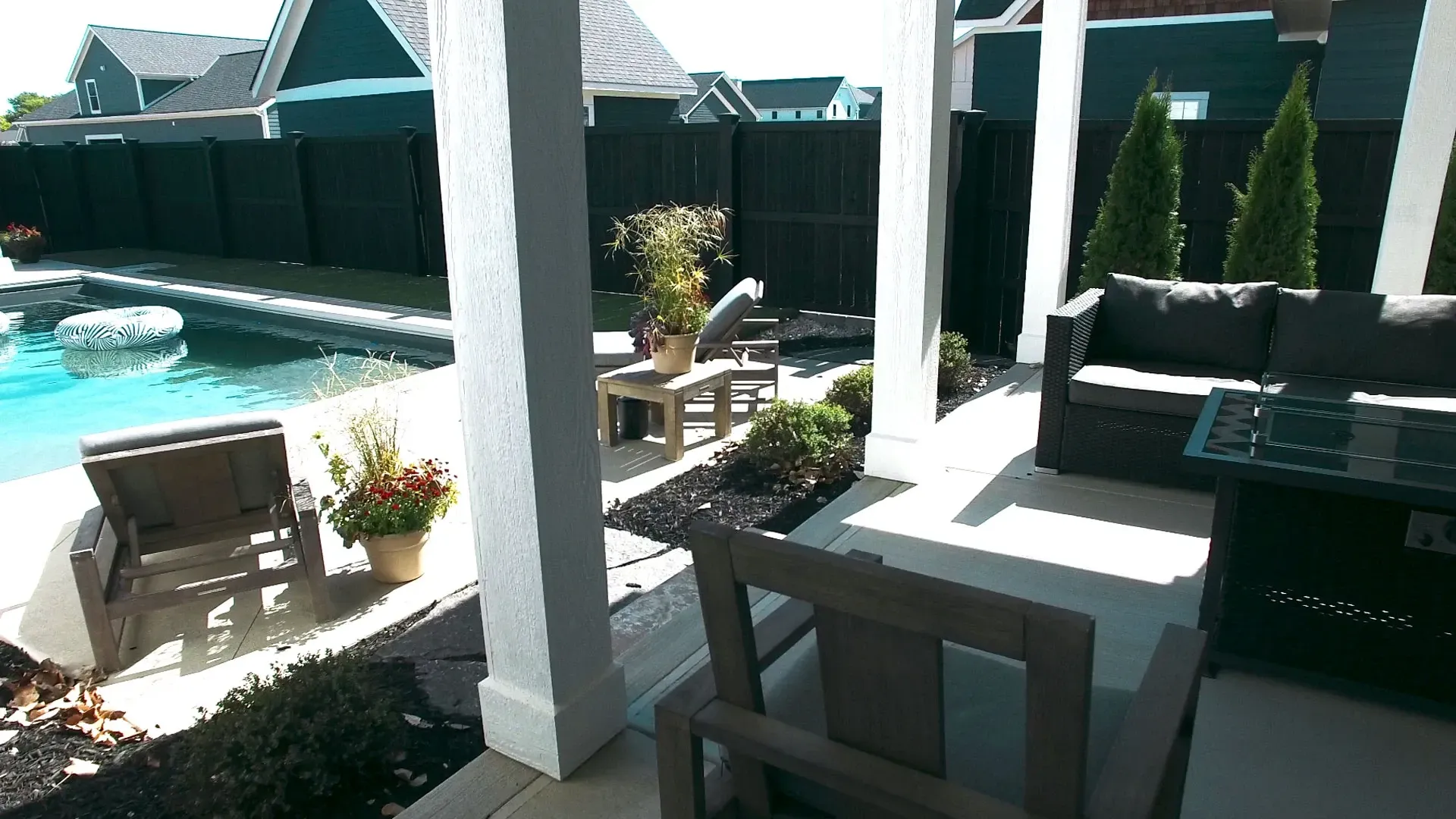 Patio with pool view: A seating area with a sofa and chair faces a swimming pool surrounded by a dark fence and trees.