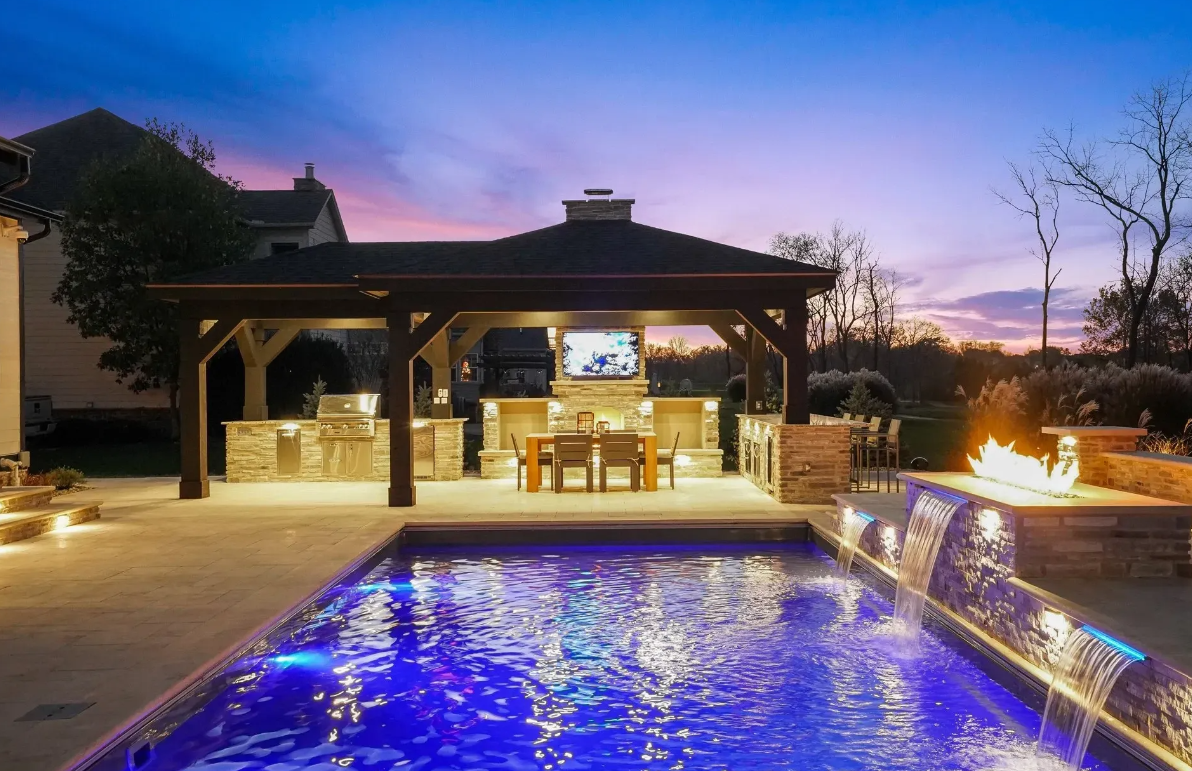 A beautifully lit backyard with a pool and gazebo, creating a serene ambiance under the night sky.
