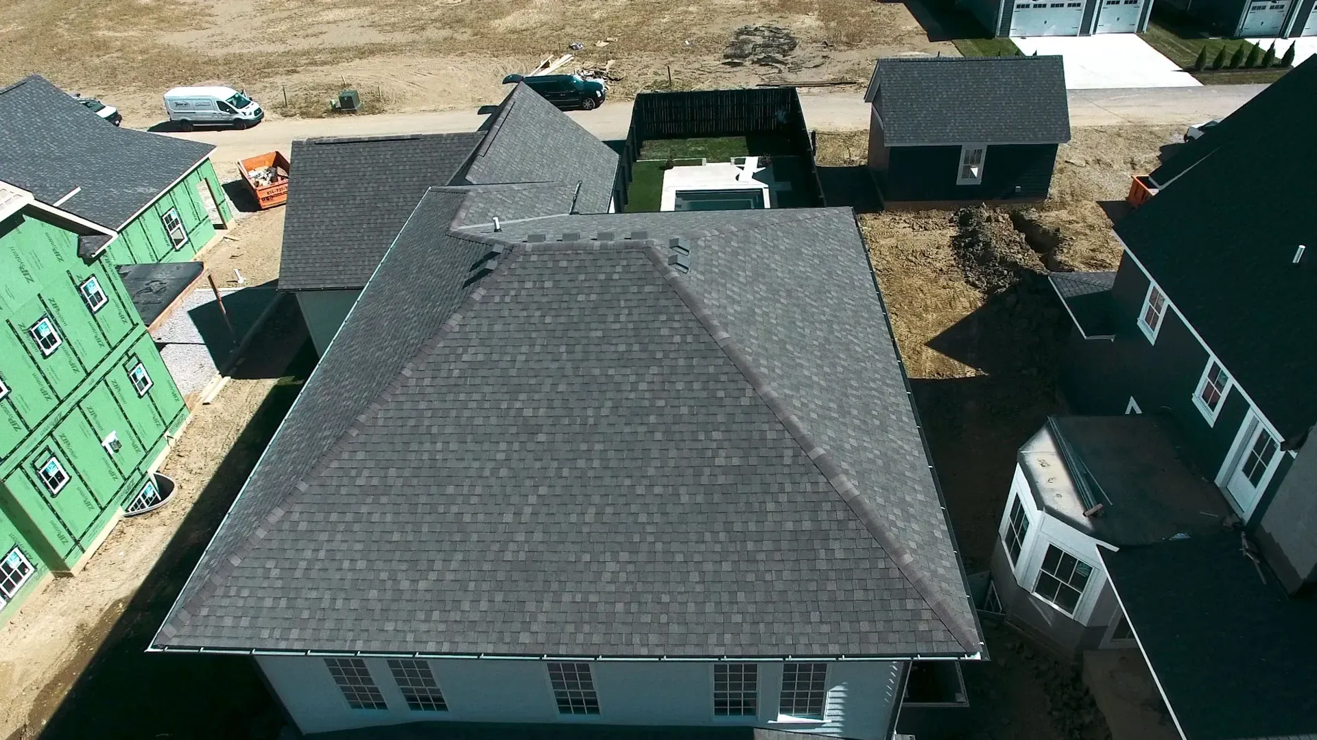 An aerial view shows a gray-roofed house and its surroundings, including other houses and a construction site.