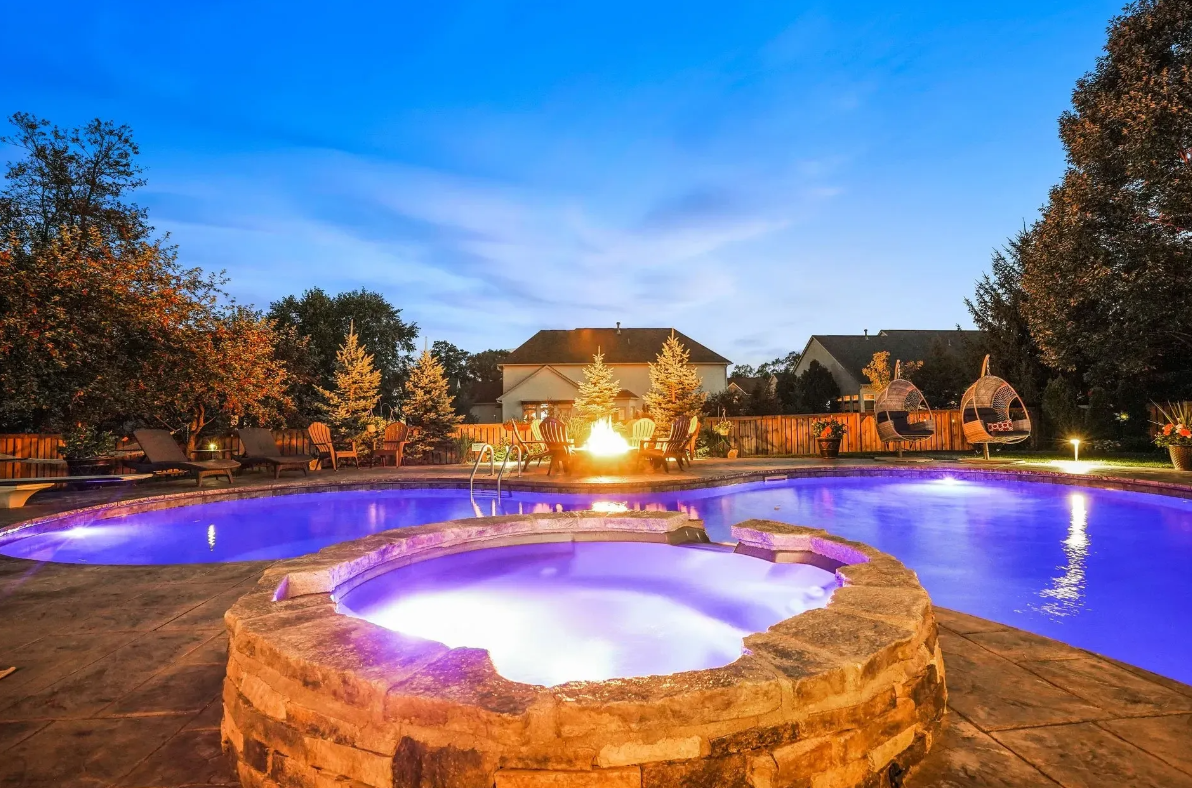 a large swimming pool with a hot tub in the middle of it at night .