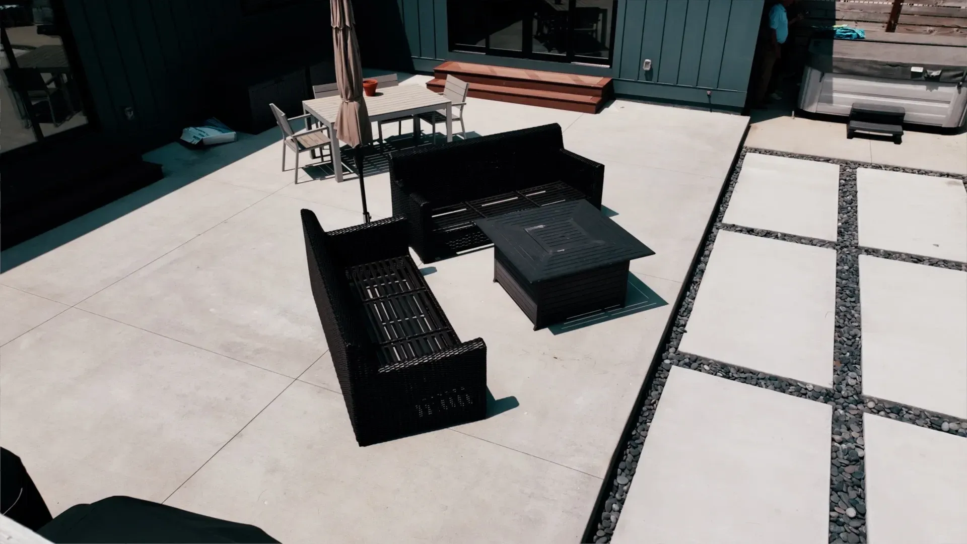 An outdoor patio with dark wicker furniture, a fire pit table, and dining set on a concrete surface.