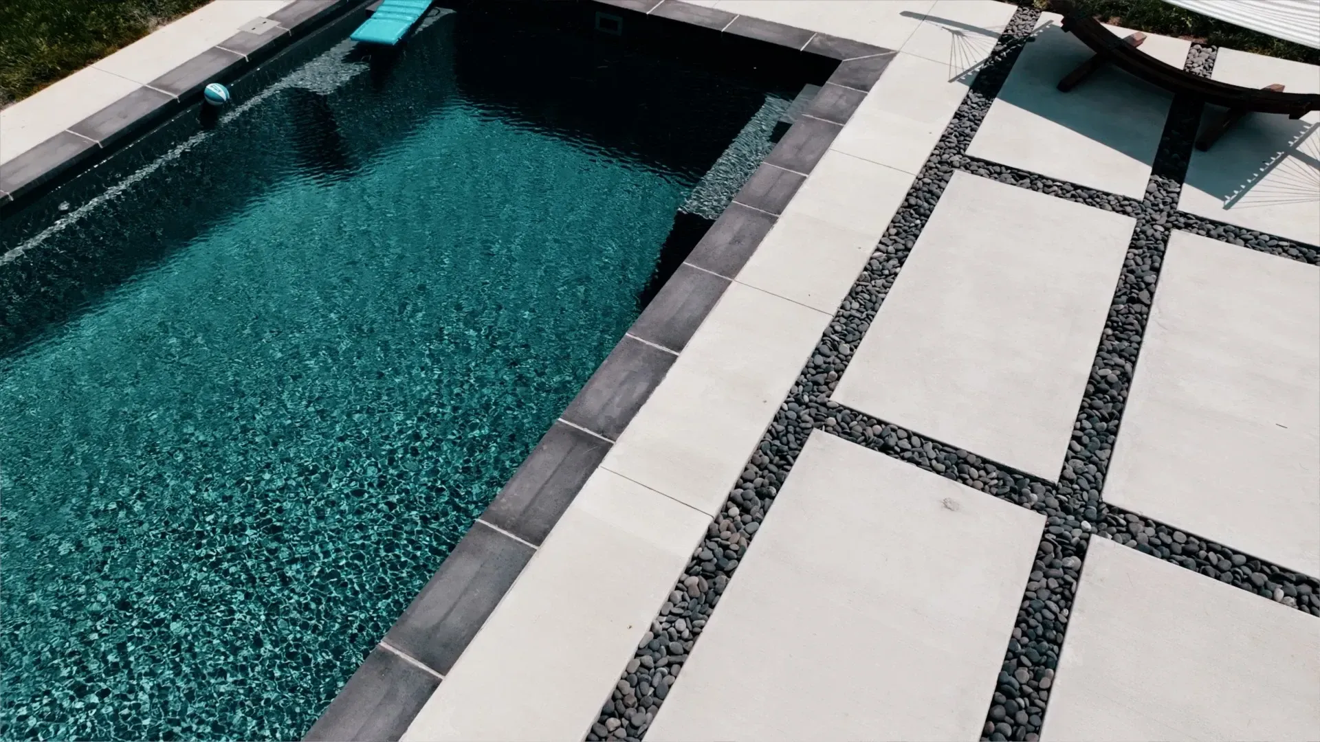 Pool with dark teal water and a gray concrete patio with black gravel accents.