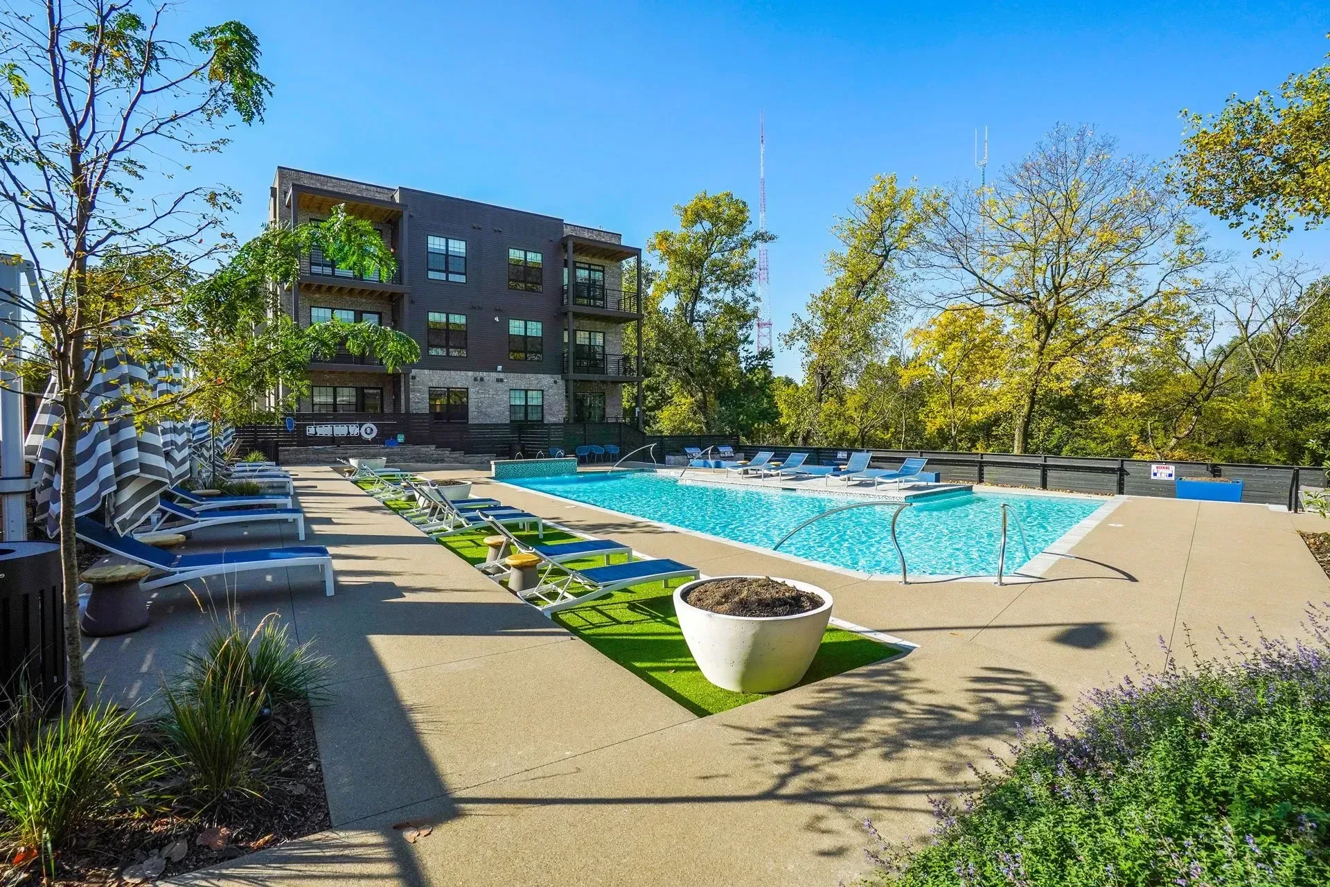 An outdoor swimming pool with lounge chairs and a modern apartment building in the background on a sunny day.