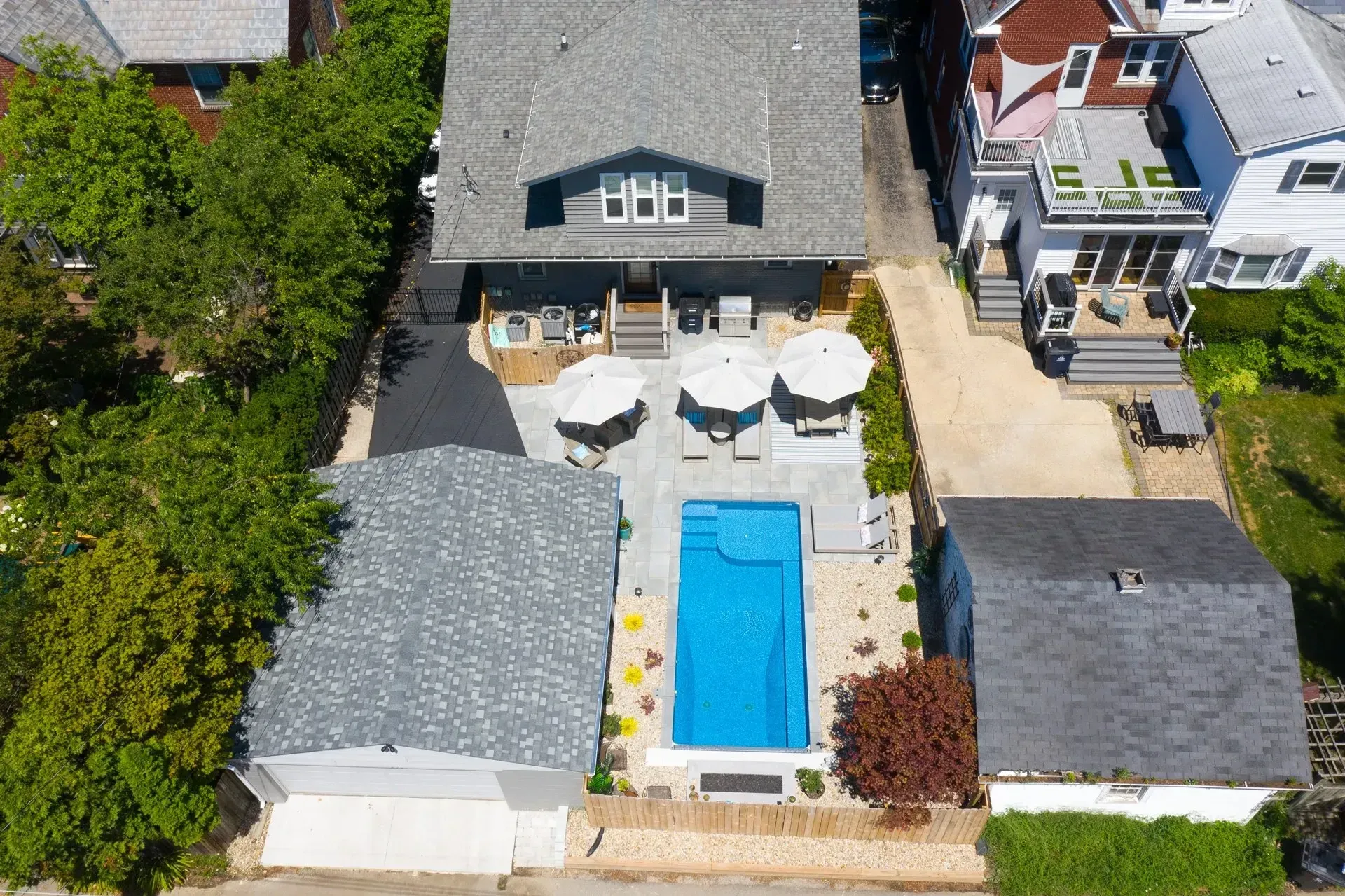 Aerial view of a house with a pool, patio, and three umbrellas. A garage and a neighboring house are visible.