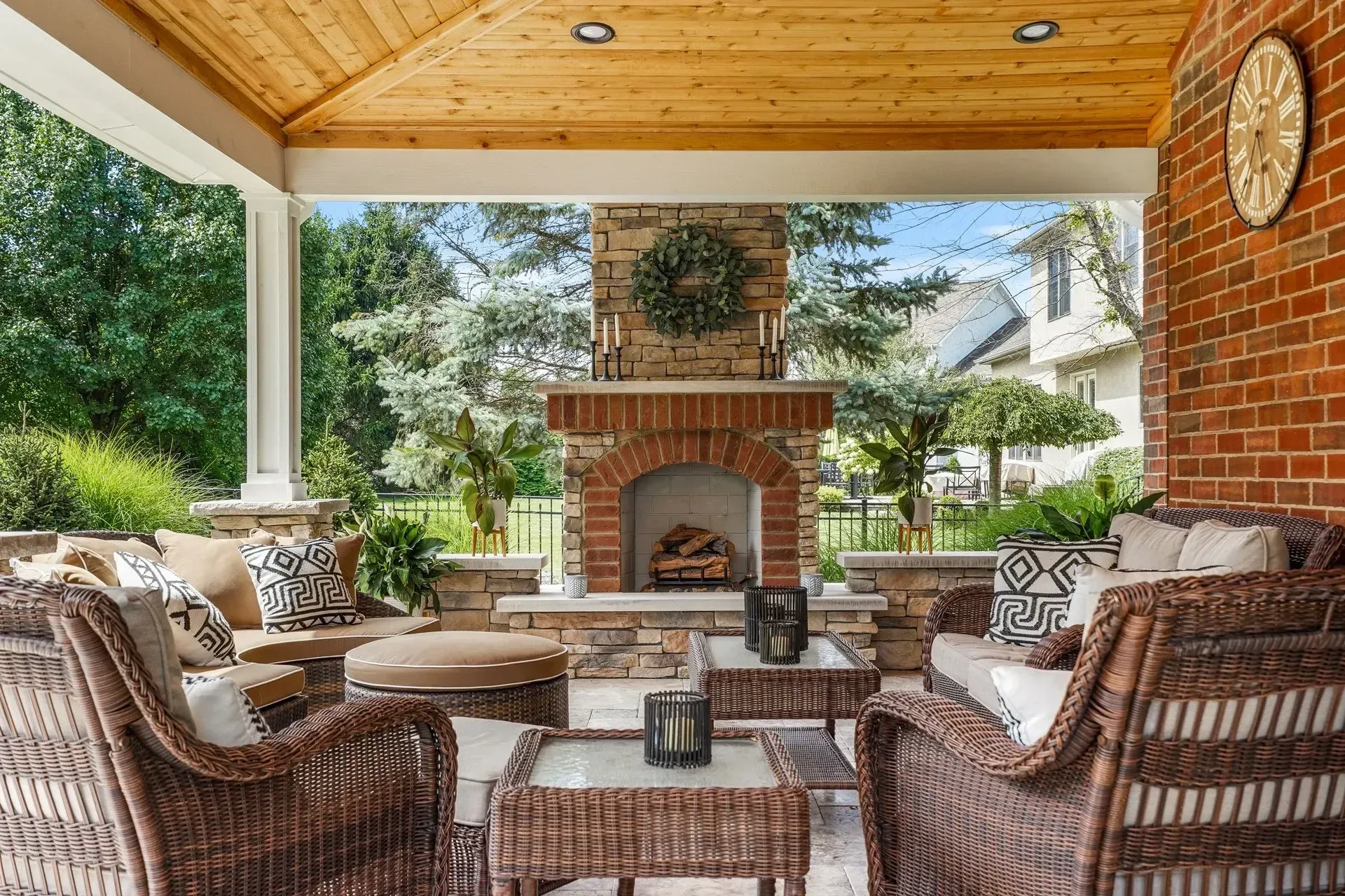Outdoor covered patio with wicker furniture, a brick fireplace, and views of a backyard.