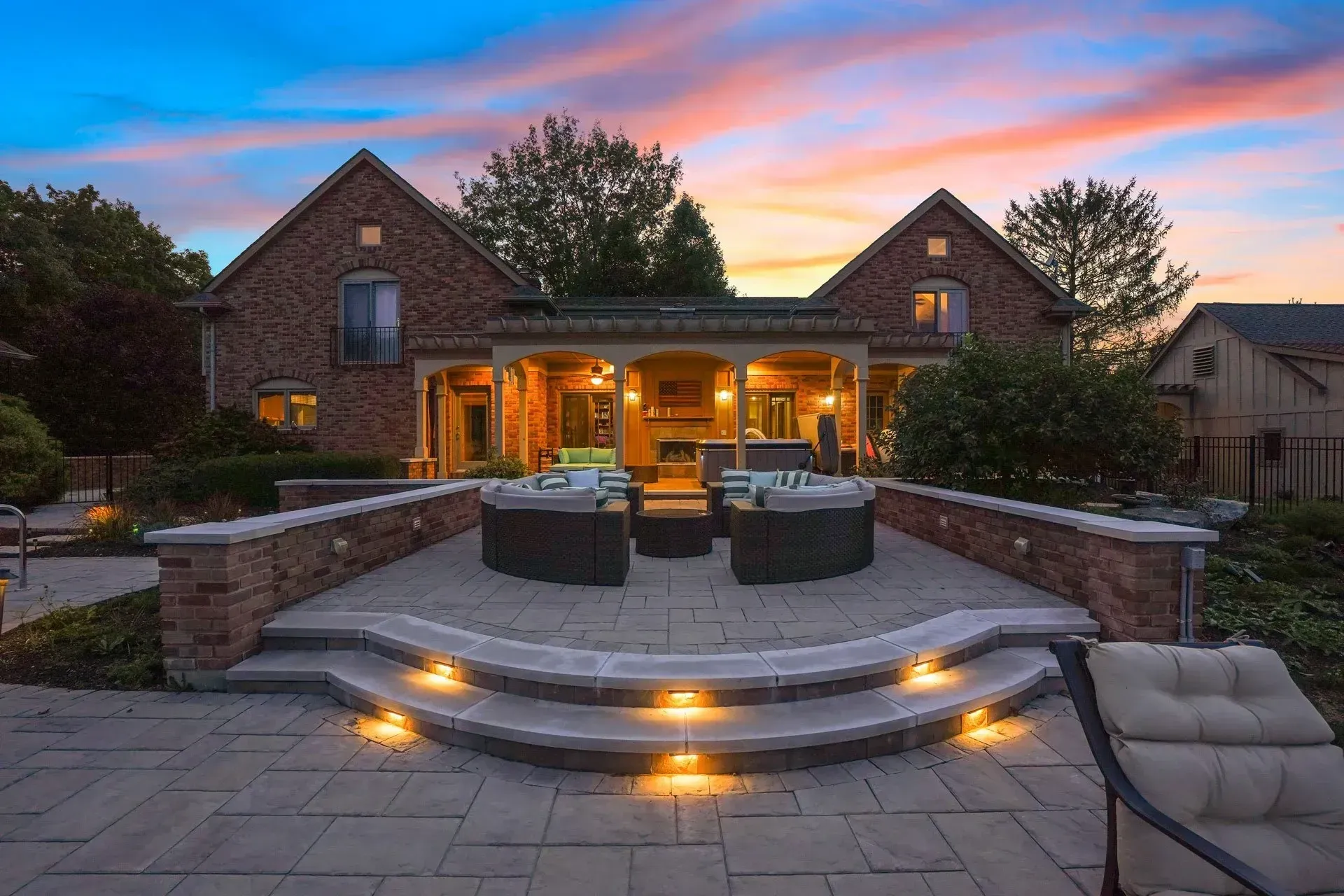 Backyard patio with brick walls and steps, outdoor seating, and a house at sunset.