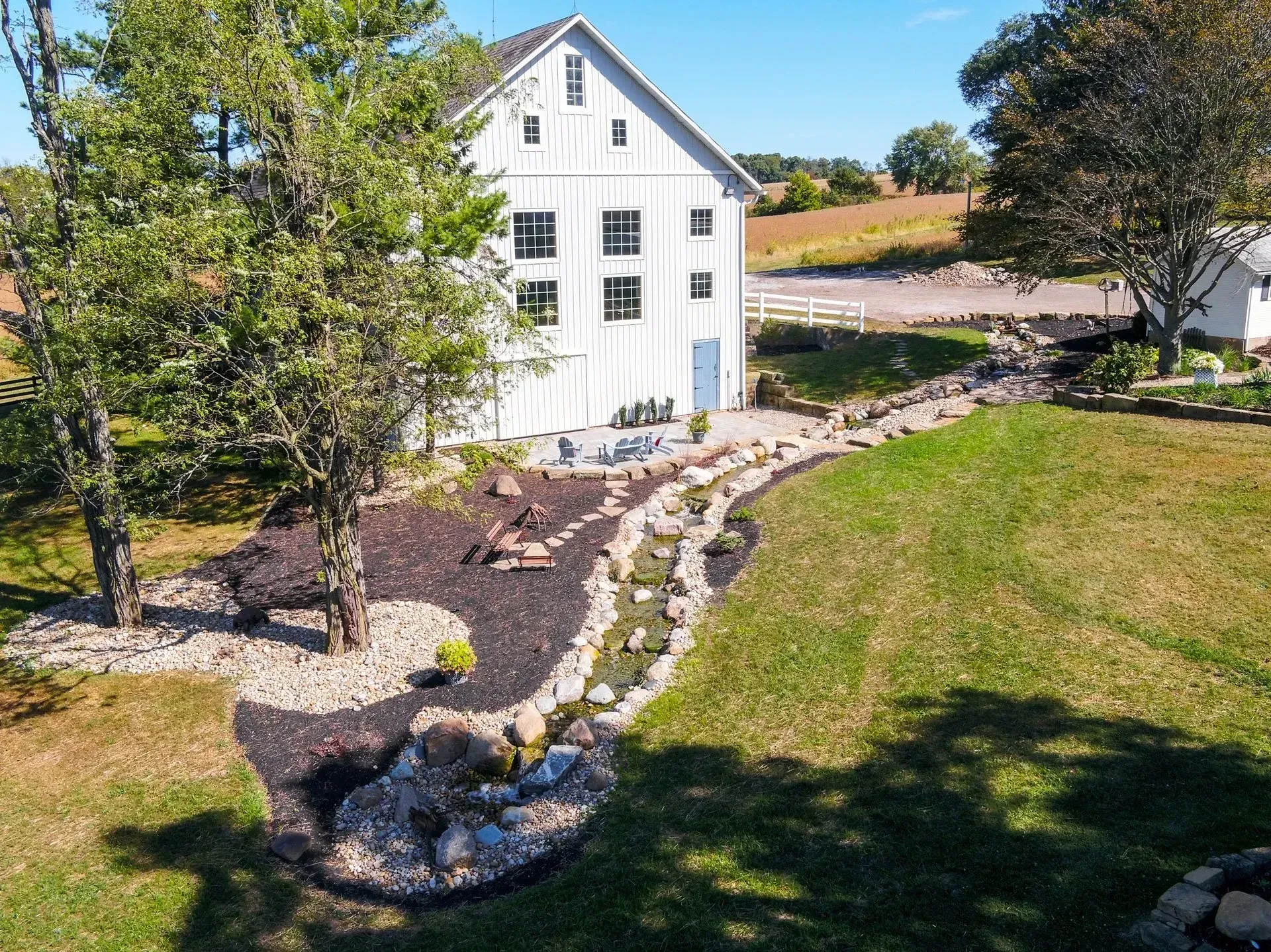 An aerial view of a white barn surrounded by trees and grass.