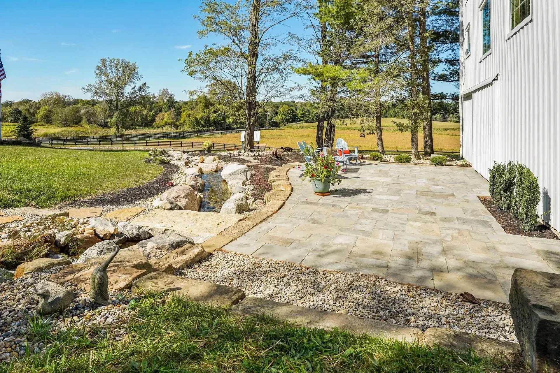 There is a patio with a view of a field and trees in the background.