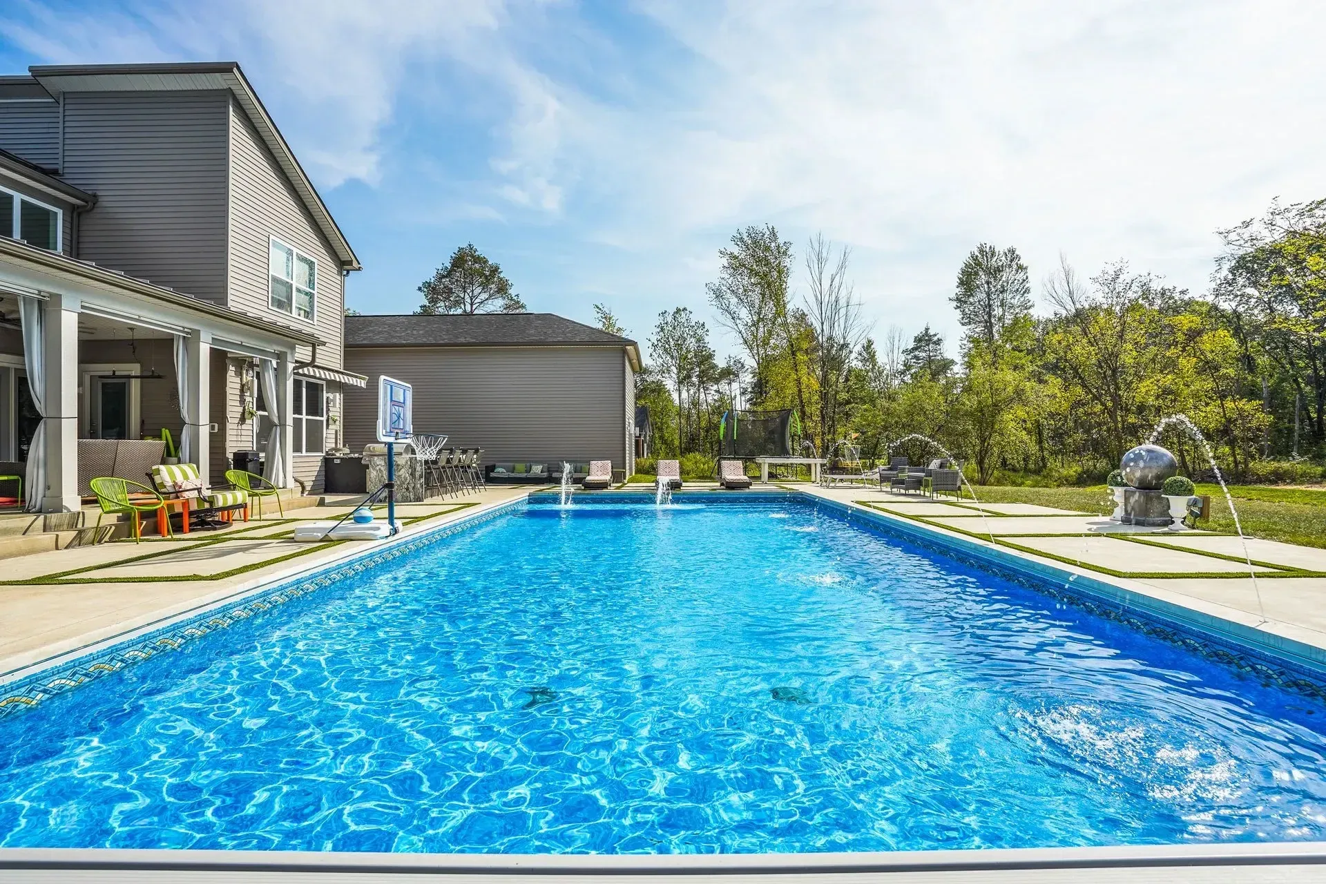 A rectangular swimming pool in a backyard next to a gray house on a sunny day.