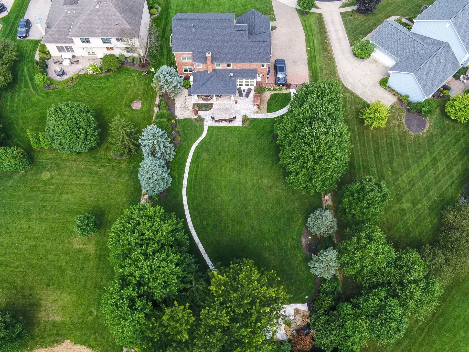 Aerial view of a large house with a backyard, lush green lawn, trees, and a curved stone pathway.