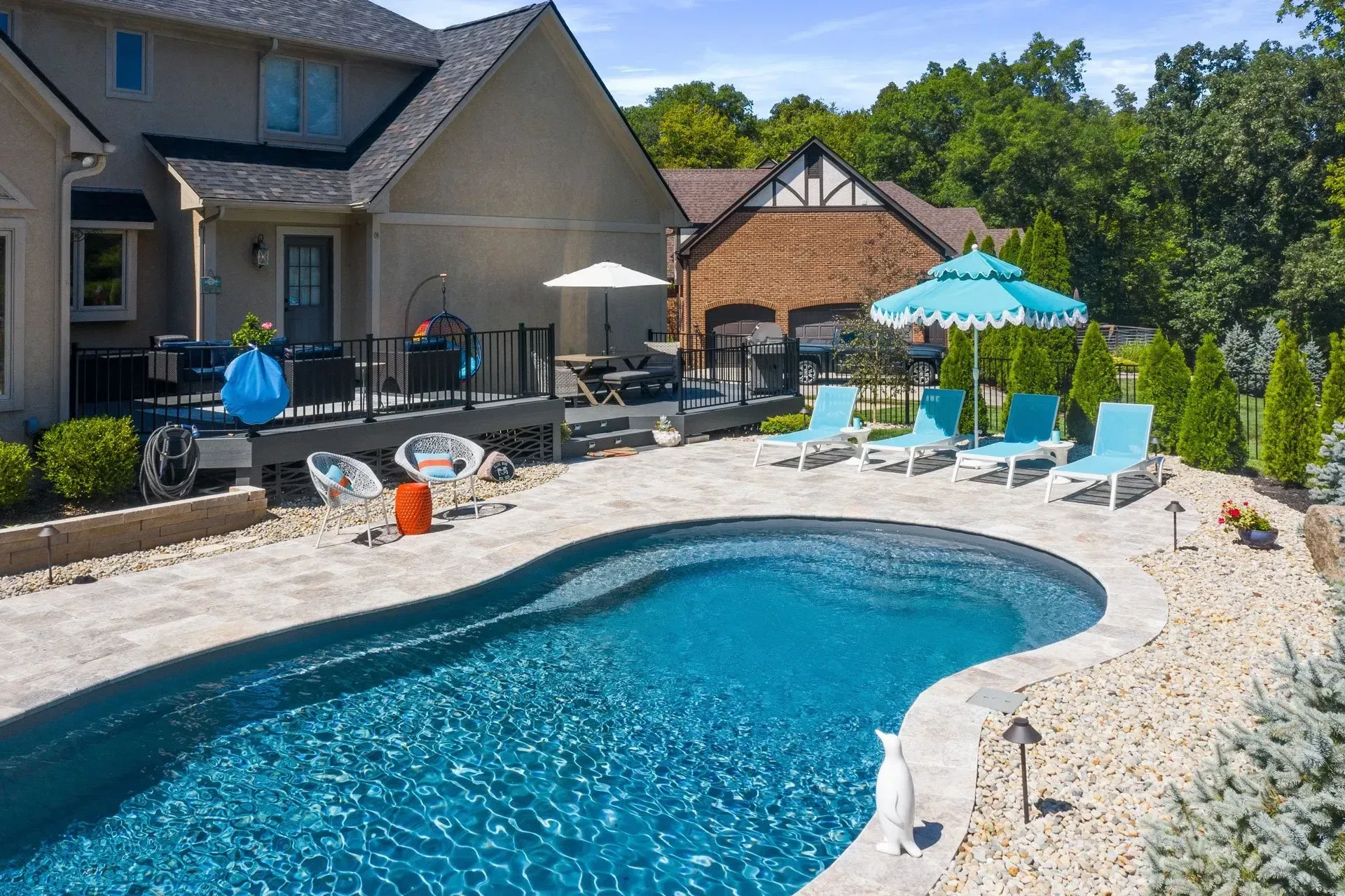 Backyard pool with blue water and lounge chairs. Houses with brown roofs and green trees in the background.
