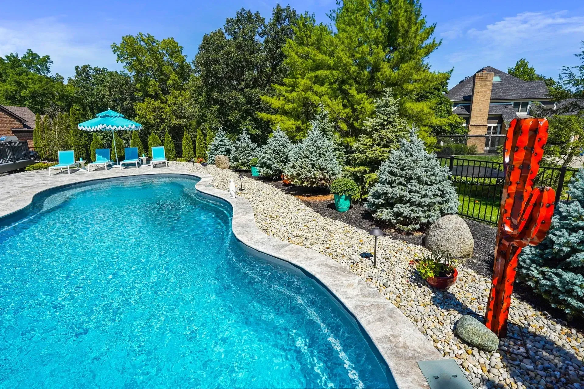 Backyard with a pool, lounge chairs, and a decorative red cactus statue. Trees and landscaping surround the pool.