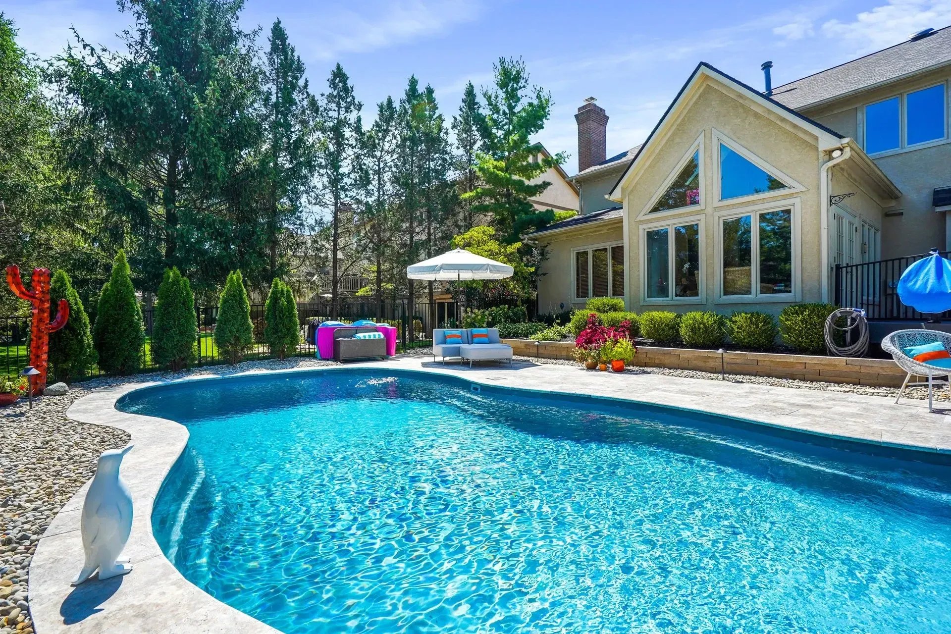 Backyard with a pool and a large house. The pool has blue water, surrounded by patio, landscaping, and outdoor furniture.