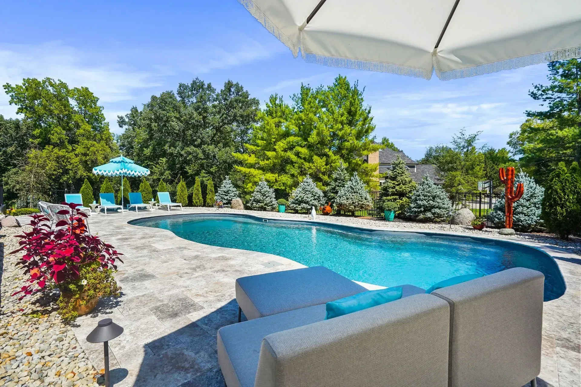 Backyard pool with lounge seating, umbrellas, and surrounding greenery on a sunny day.
