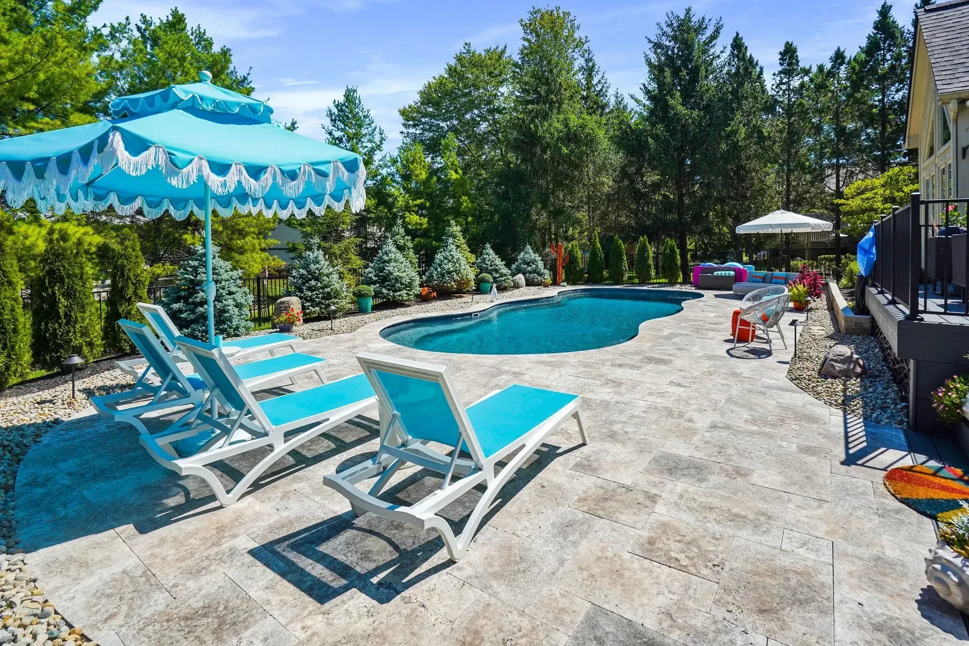 Poolside scene with a blue umbrella, lounge chairs, and a pool on a sunny day.