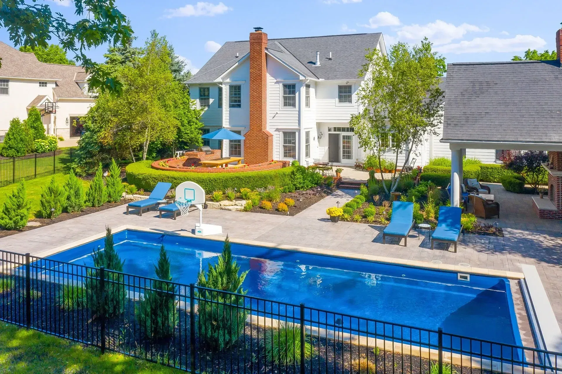 Backyard with a rectangular blue pool, lounge chairs, landscaping, and a two-story white house.
