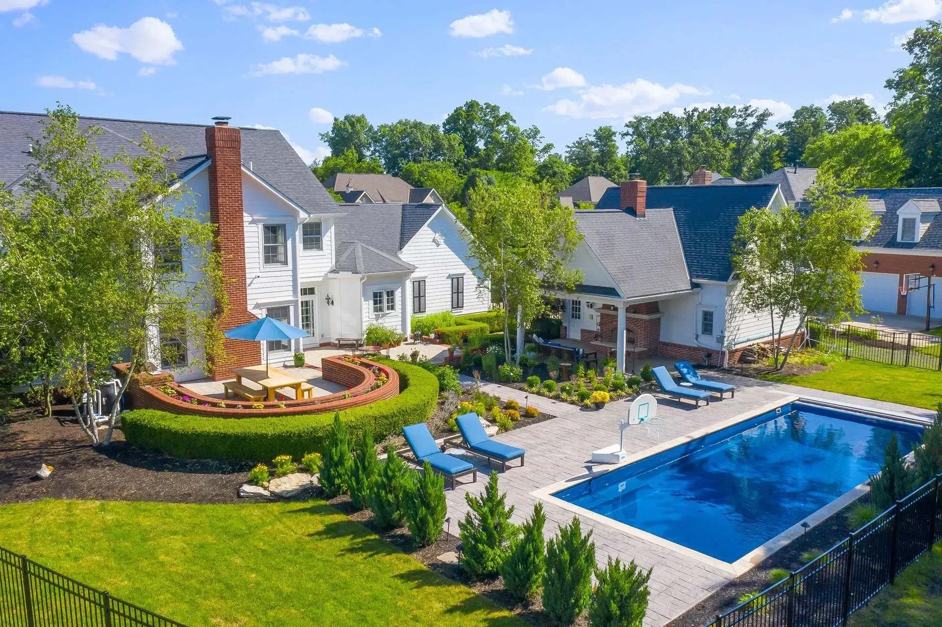 Aerial view of a white house with a pool, patio, fire pit, and manicured lawn in a sunny setting.