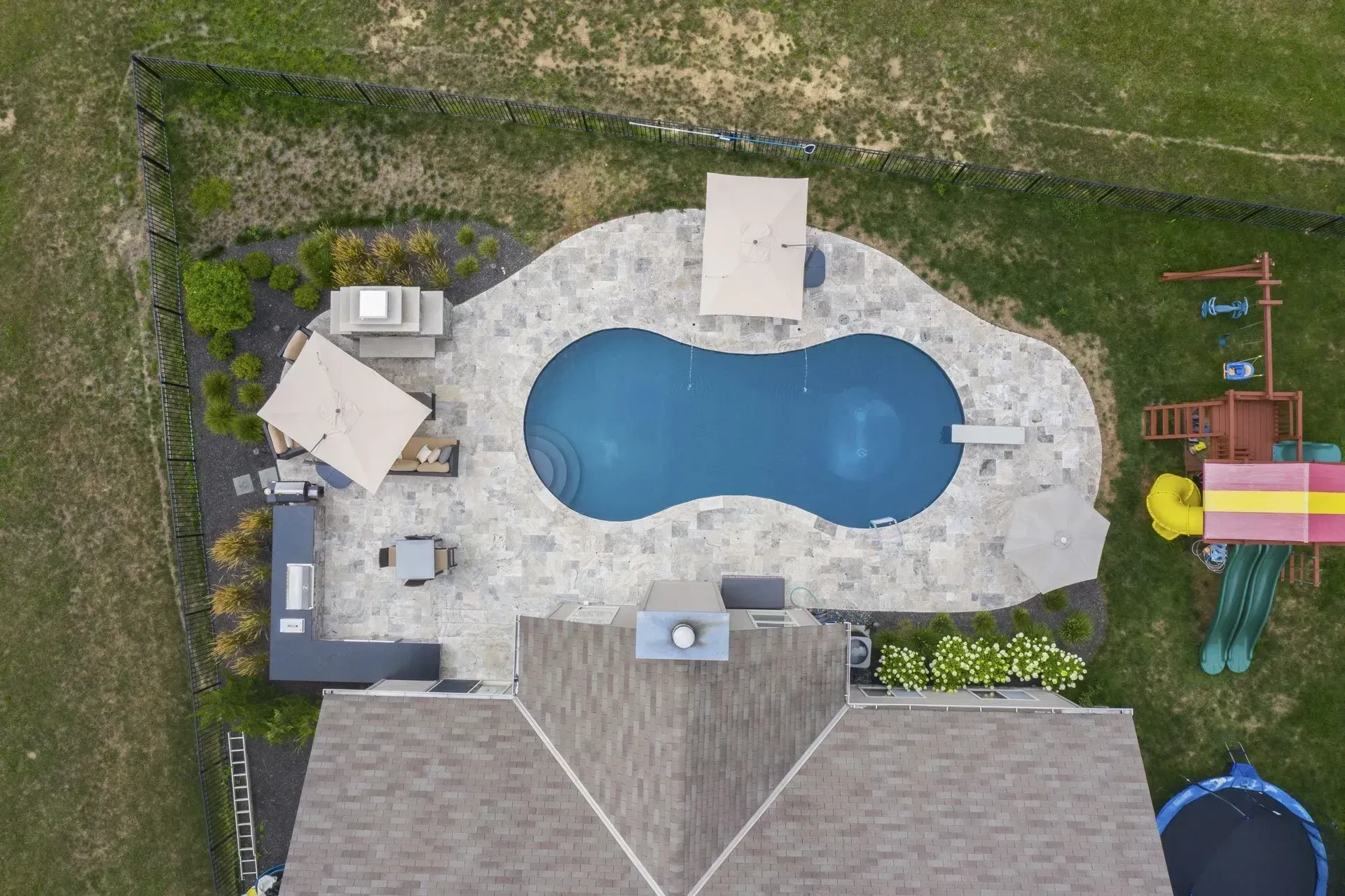 An aerial view of a house with a large swimming pool and a playground.