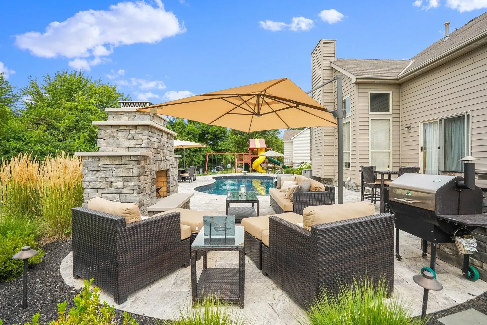 A patio with a grill , umbrella , chairs and a fireplace.
