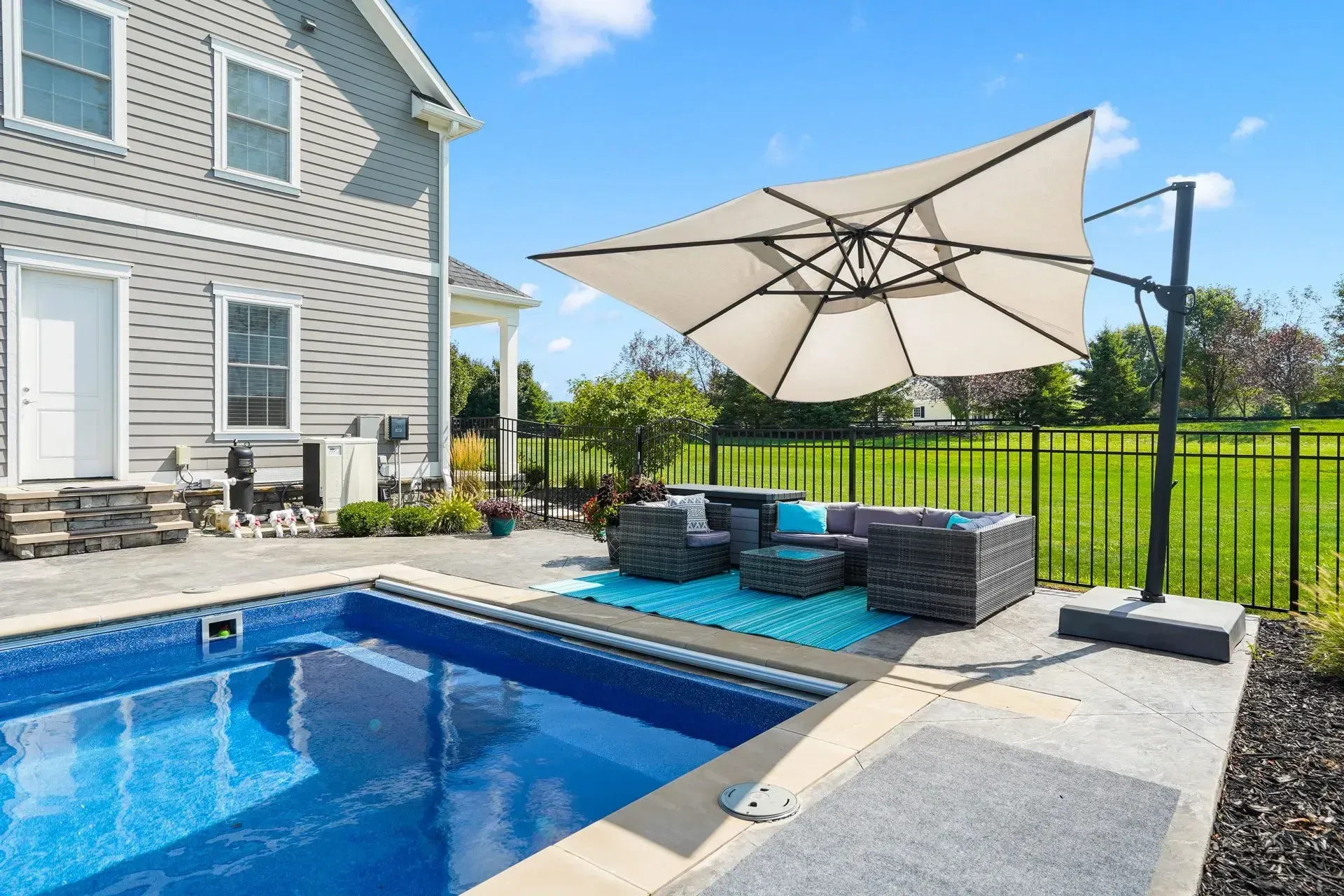 A backyard with a pool, patio furniture, and a large umbrella next to a house on a sunny day.