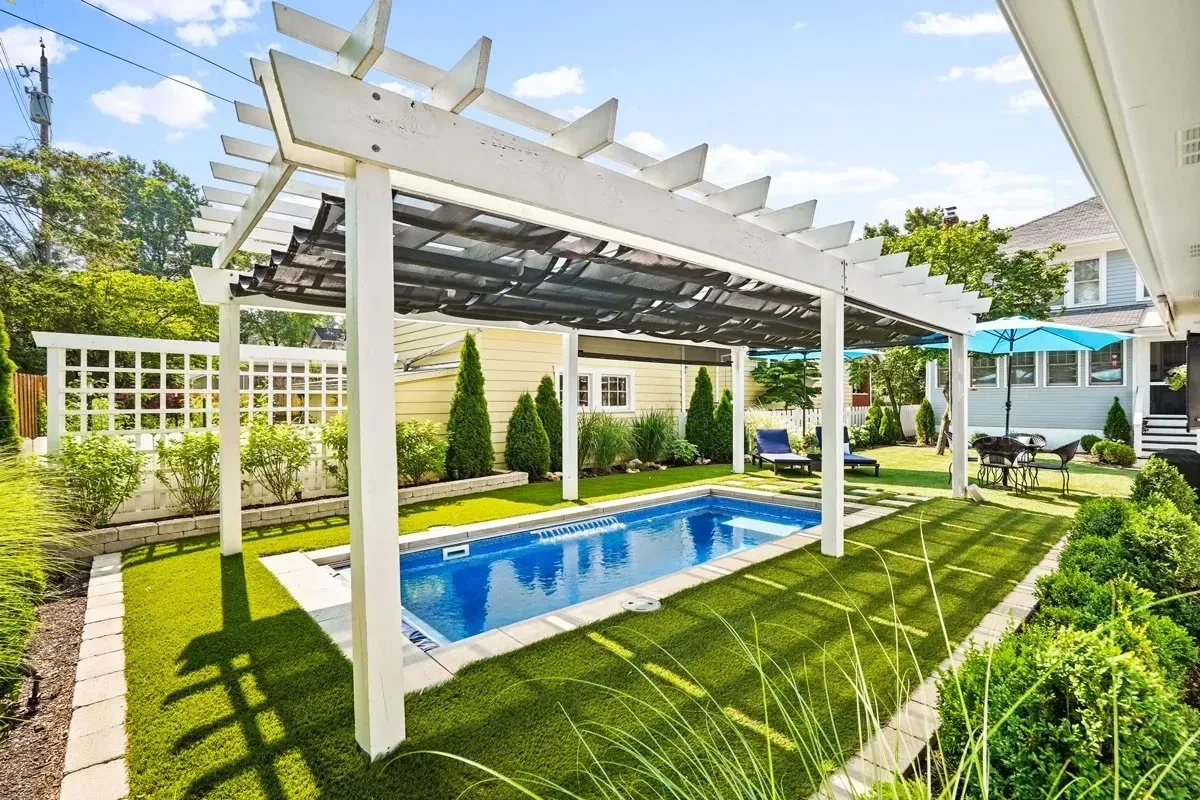 A white pergola over a swimming pool in a backyard.