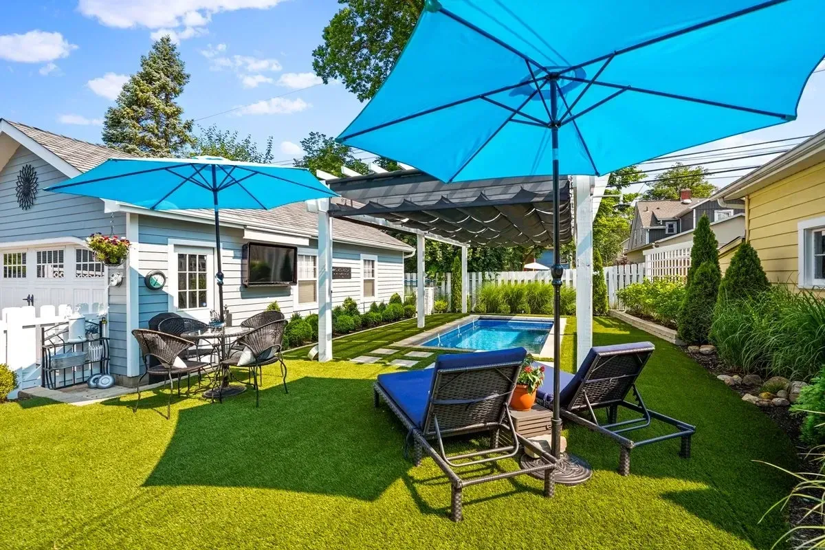A backyard with umbrellas , chairs and a pool.