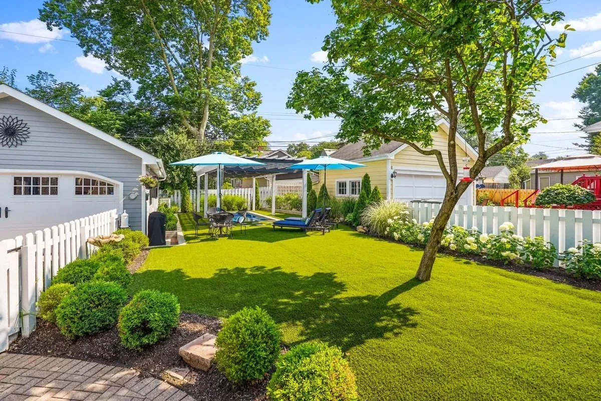 A lush green yard with a white picket fence and a house in the background.