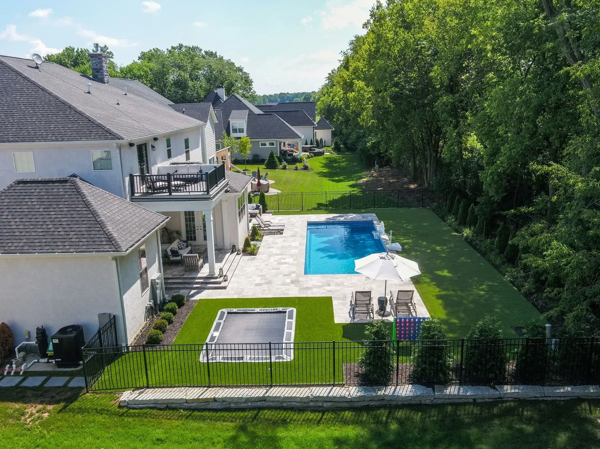 Aerial view of a white luxury home with a pool and patio. Green grass surrounds the pool and a black fence borders the yard.