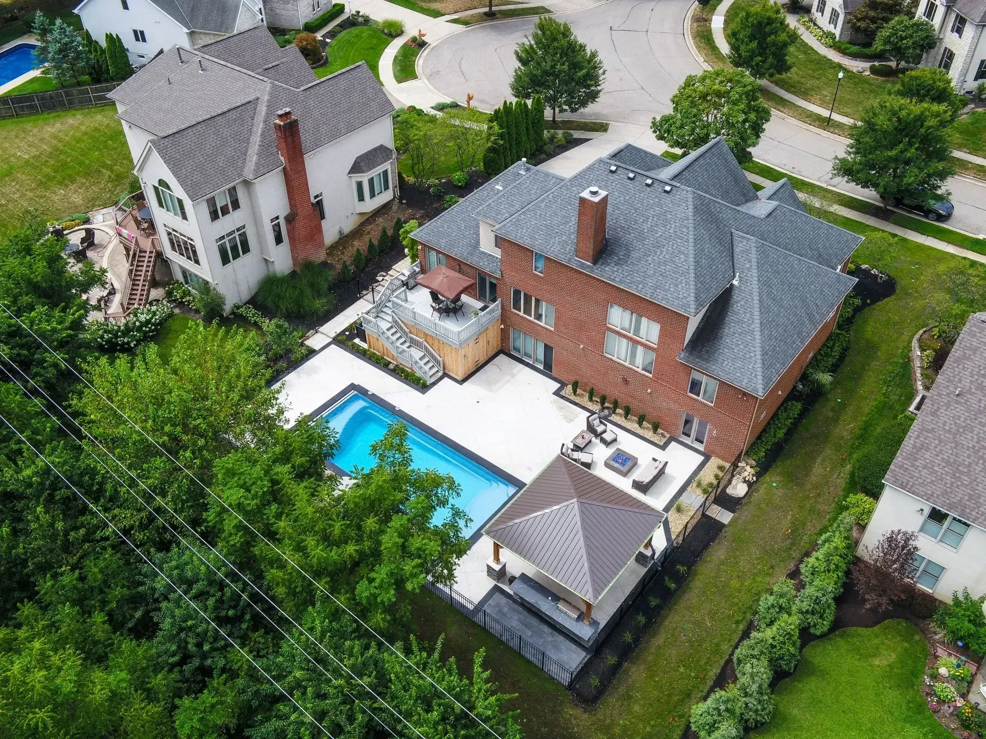 Aerial view of a large brick house with a pool, patio, and gazebo. Lush green landscaping surrounds the property.