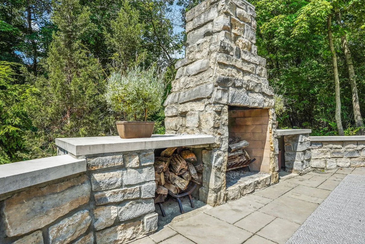 An outdoor stone fireplace stands in the center of a backyard, providing warmth and ambiance to the outdoor space.