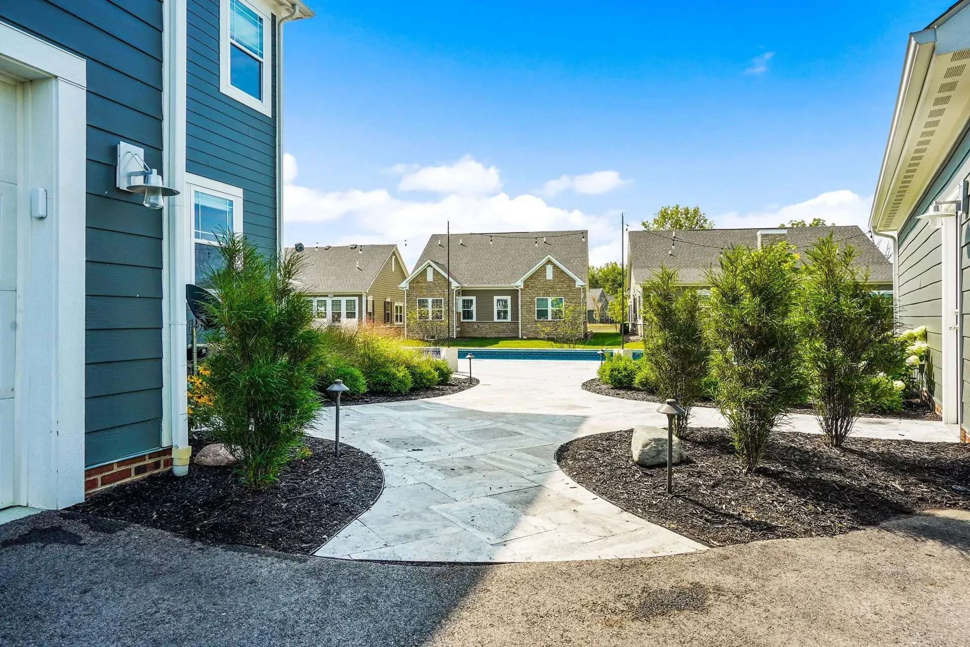 A walkway between two houses with a pool in the background