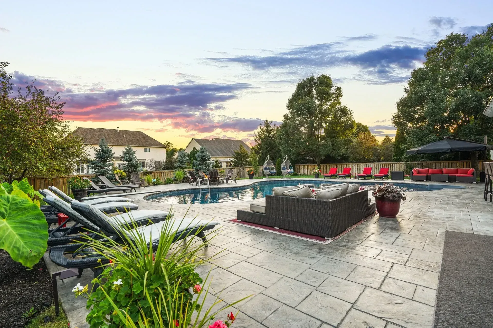 Luxury backyard with a swimming pool and lounge area at sunset. Includes lounge chairs, a hot tub, and lush landscaping.