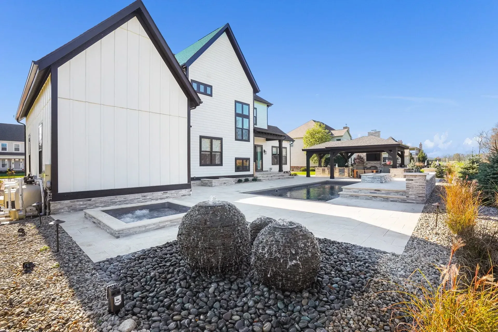 Backyard with a pool, hot tub, and modern farmhouse style home. Black and white exterior with a stone patio.