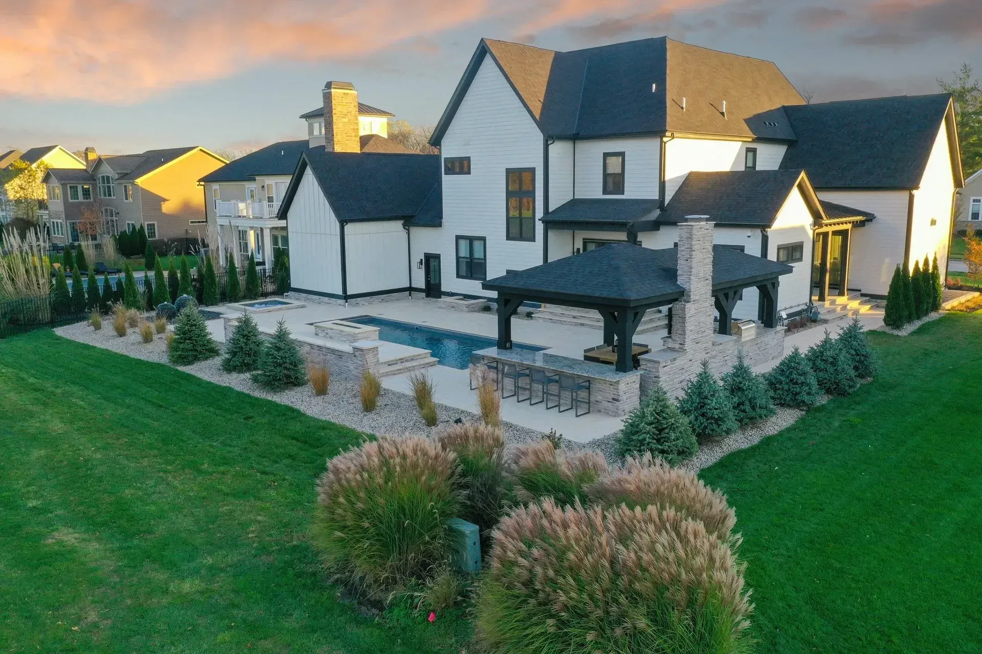 A modern, two-story white house with black trim, a pool, and patio with a pergola in a grassy yard.