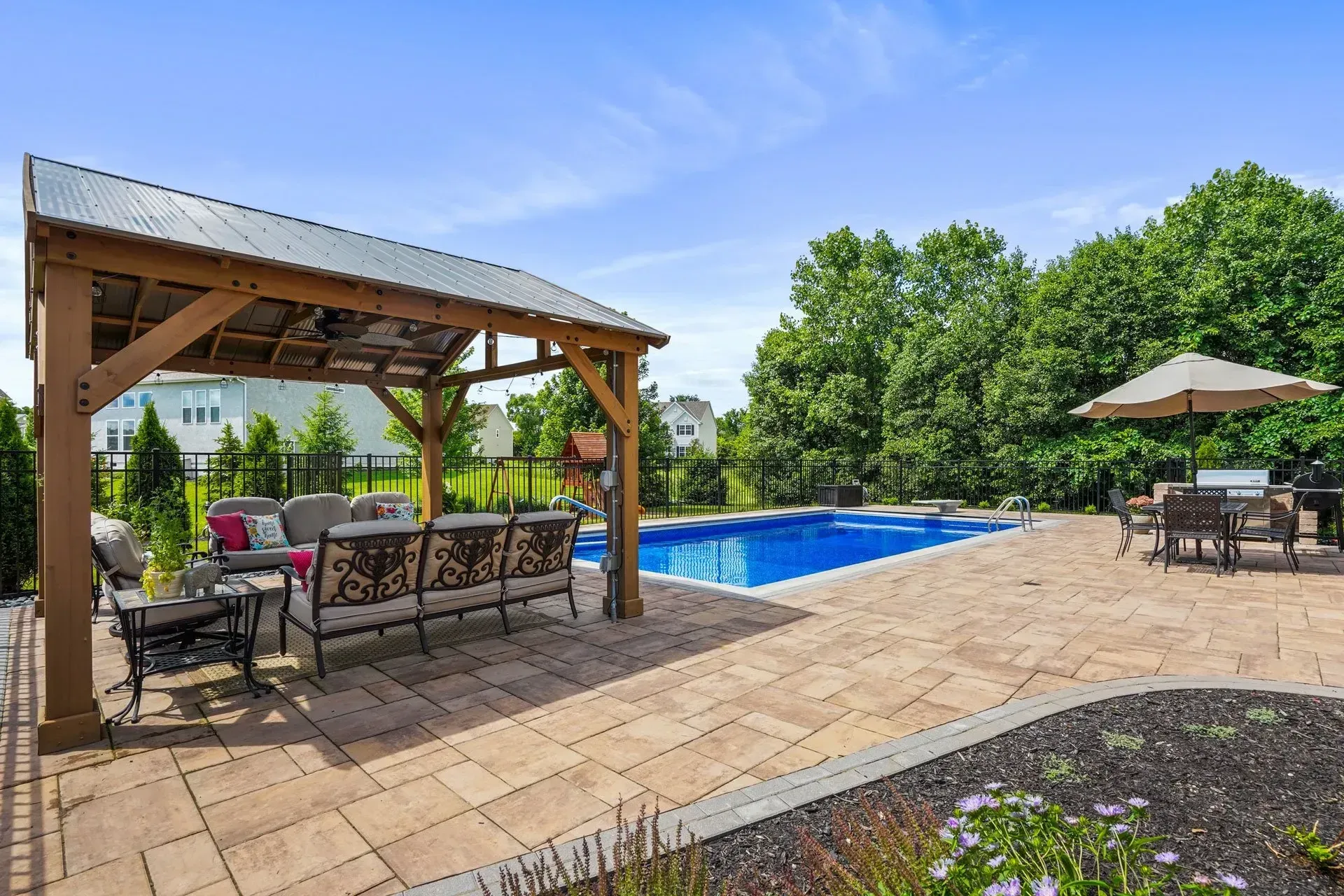 Backyard patio with a pool, seating under a wooden pergola, and a dining area with an umbrella.