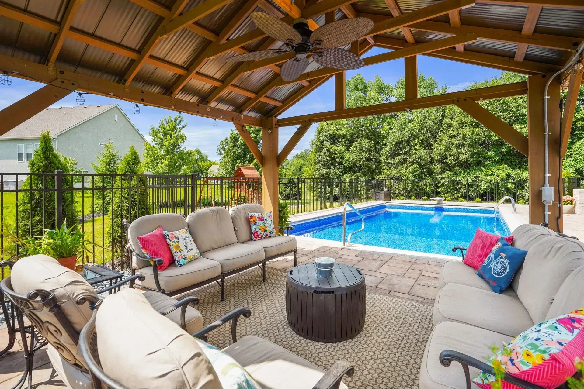 Outdoor patio with a pool: a seating area under a wooden pergola with a pool in the background.
