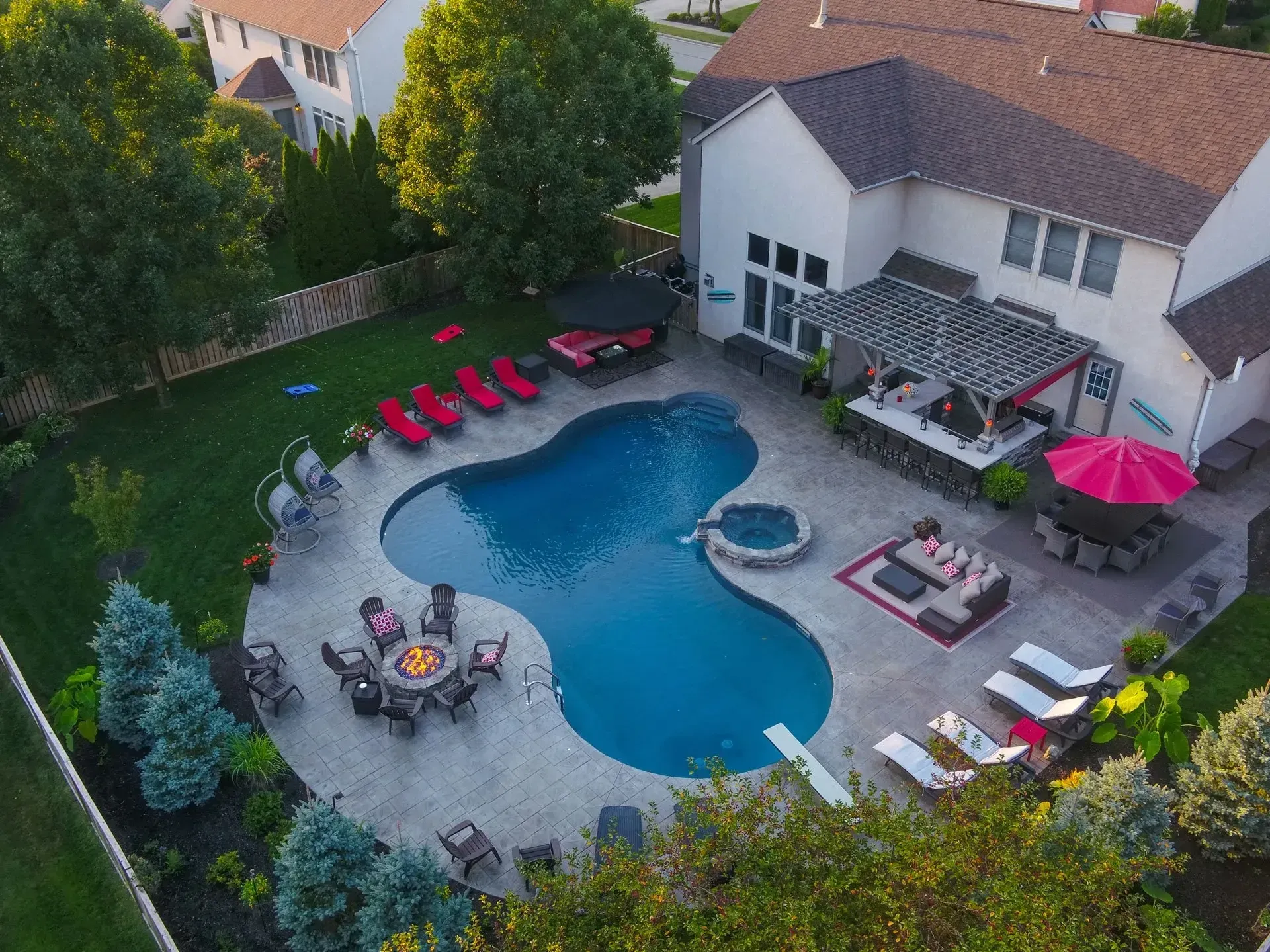 Aerial view of a backyard with a freeform pool, patio, and outdoor living spaces. Includes a bar, lounge chairs, and fire pit.