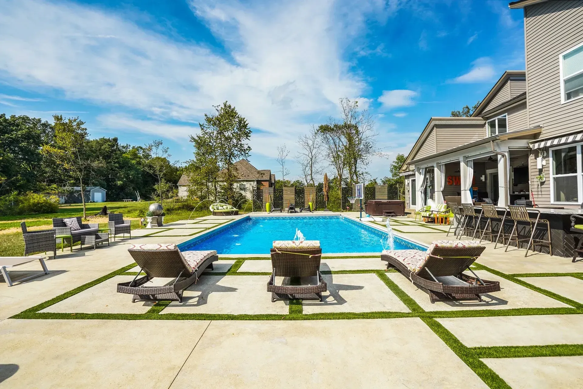 Backyard with a rectangular pool, lounge chairs, and a house with a sunny blue sky overhead.