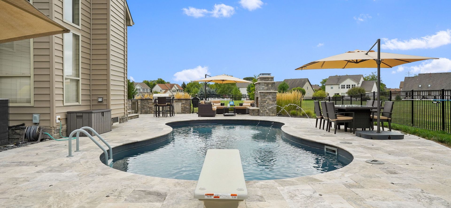 Backyard with a pool, patio, and outdoor dining area on a sunny day. A diving board sits over the pool.