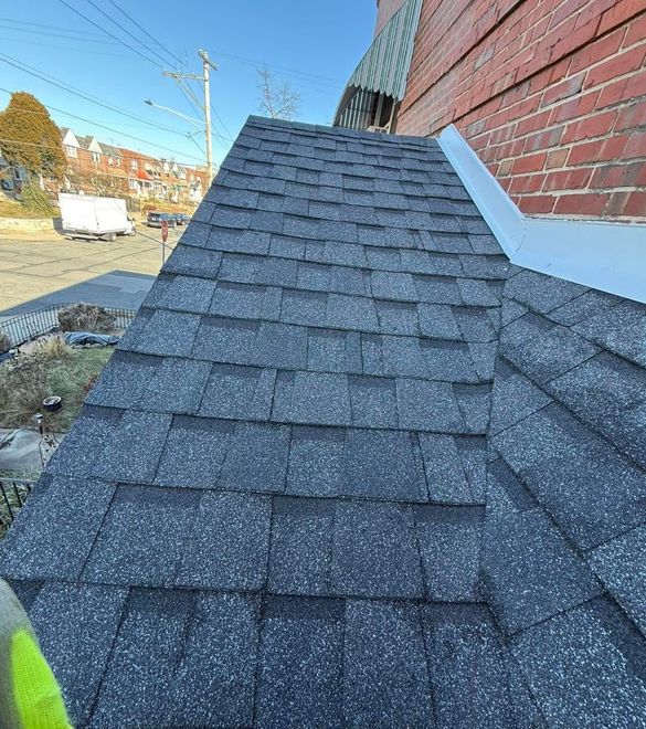 Close-up of a dark gray shingle roof beside a red brick wall on a sloped building.