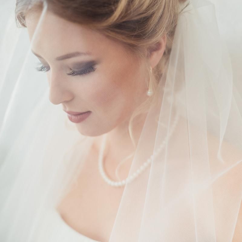 Sposa con velo e collana di perle, sguardo rivolto verso il basso.