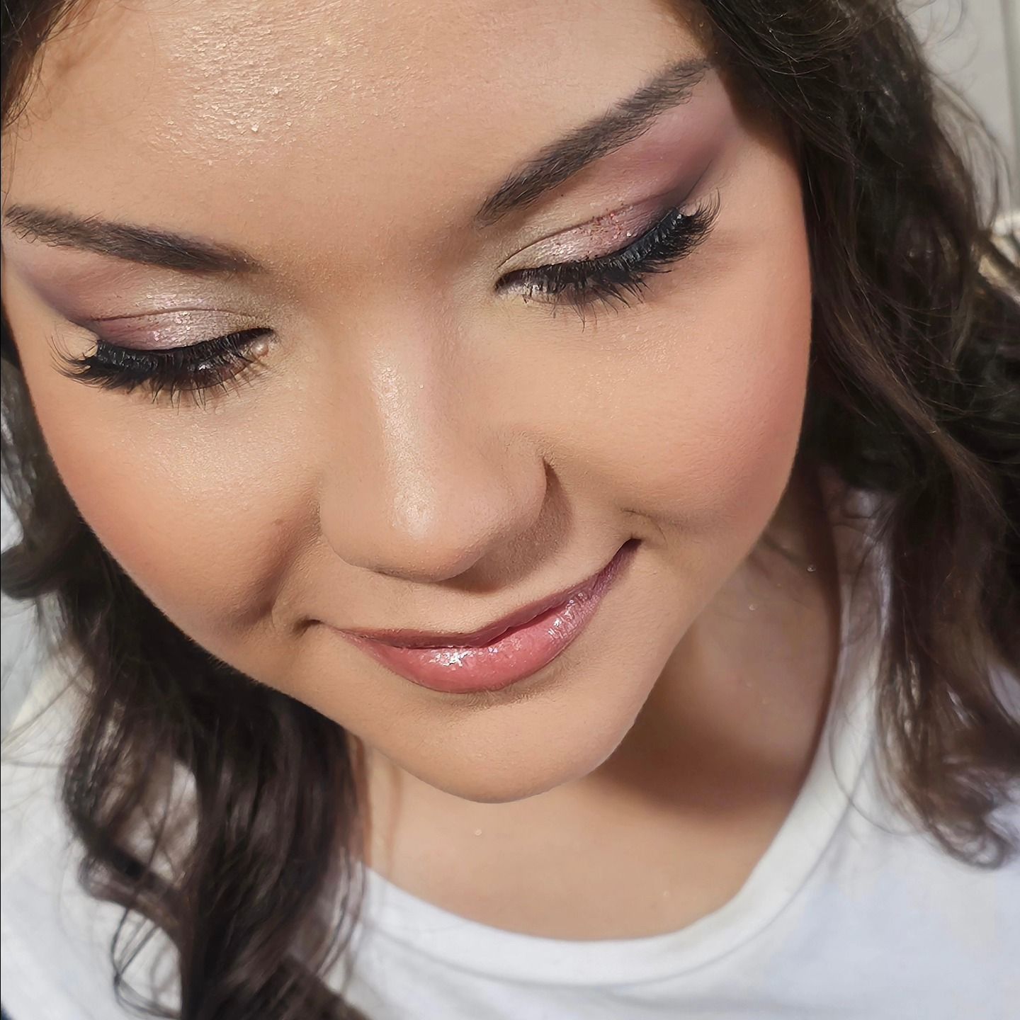 Donna con capelli scuri e ricci, truccata con ombretto rosa e argento, fard rosa e rossetto rosa.